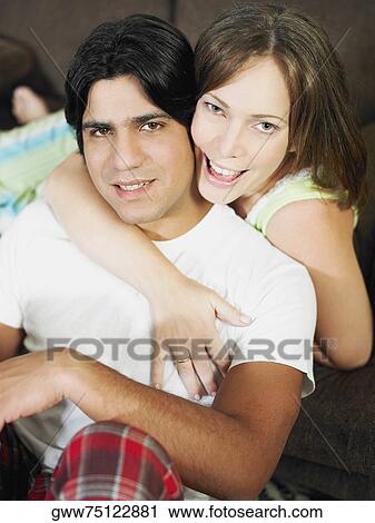 Stock Image - Portrait of a young woman embracing a young man from behind and smiling. Fotosearch