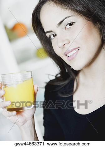 Stock Image - Portrait of a young woman holding a glass of orange juice and smiling. Fotosearch