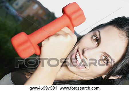 Stock Image - Portrait of a young woman holding a hand weight. Fotosearch