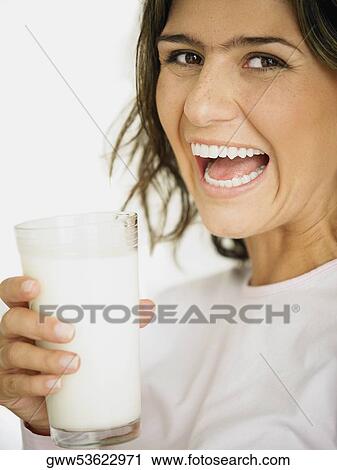 Stock Image - Portrait of a young woman holding a glass of milk and laughing. Fotosearch