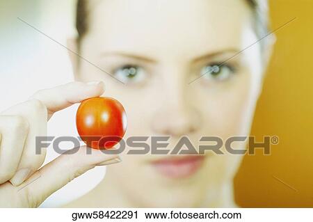 Stock Image - Portrait of a young woman holding a tomato. Fotosearch