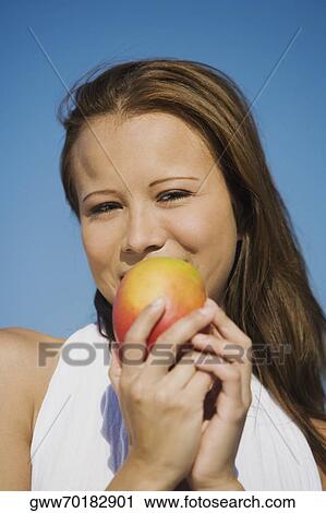 Stock Image - Portrait of a young woman holding a mango and smiling. Fotosearch