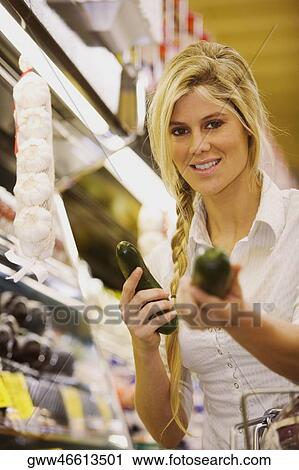 Stock Image - Portrait of a young woman holding two cucumbers and smiling. Fotosearch