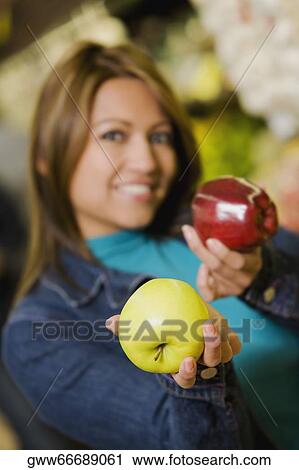 Stock Image - Portrait of a young woman holding two apples and smiling. Fotosearch