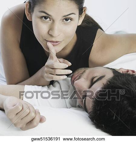 Stock Image - Portrait of a young woman lying on a young man with her finger on her lips. Fotosearch