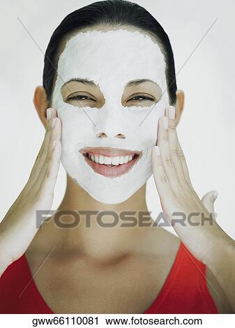 Stock Image - Portrait of a young woman smiling with a facial mask on her face. Fotosearch
