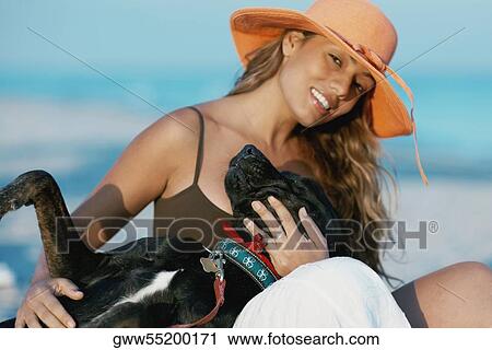 Stock Image - Portrait of a young woman stroking a dog on the beach. Fotosearch