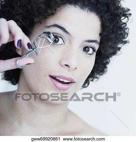 Stock Image - Portrait of a young woman using an eyelash curler. Fotosearch
