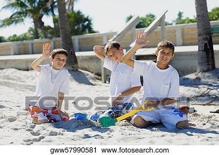 Stock Image - Portrait of two boys and a teenage boy playing with sand pail and shovel on the beach. Fotosearch