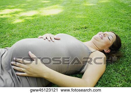 Pregnant young woman lying on the grass and touching her abdomen View Large Photo Image Stock Image - Pregnant young woman lying on the grass and touching her abdomen. Fotosearch