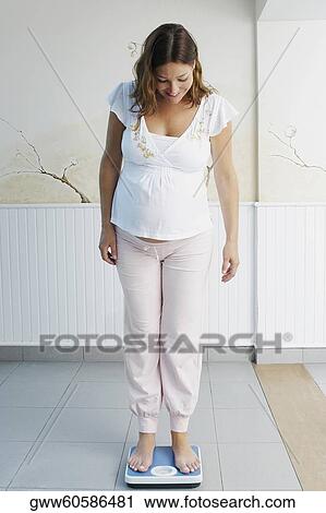 Pregnant young woman standing on a weighing scale View Large Photo Image Stock Image - Pregnant young woman standing on a weighing scale. Fotosearch