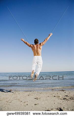 Stock Image - Rear view of a man jumping on the beach. Fotosearch