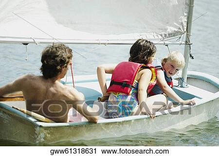 Stock Image - Rear view of a mid adult man with his children in a sailboat. Fotosearch