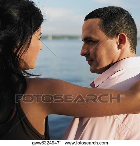 Rear view of a young couple sitting on a pier with their arms around each other View Large Photo Image Stock Image - Rear view of a young couple sitting on a pier with their arms around each other. Fotosearch