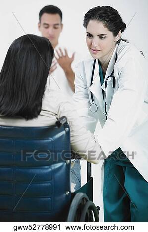 Stock Image - Rear view of female patient sitting on a wheelchair and talking to a female doctor. Fotosearch