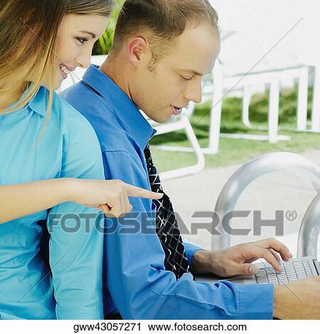 Stock Image - Side profile of a businessman using a laptop with a teenage girl sitting behind him. Fotosearch