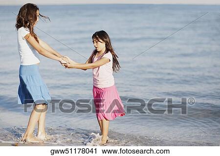 Stock Image - Side profile of a girl holding hands of her sister on the beach. Fotosearch