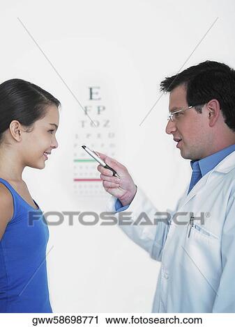Stock Image - Side profile of a male doctor doing an eye exam of a female patient. Fotosearch