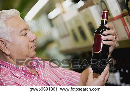 Stock Image - Side profile of a mature man holding a wine bottle. Fotosearch