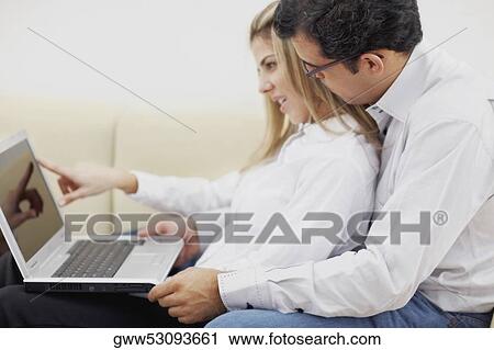 Stock Image - Side profile of a mid adult couple using a laptop. Fotosearch