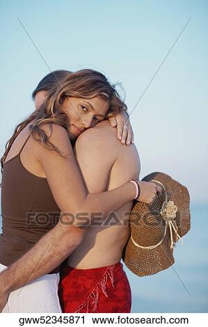 Stock Image - Side profile of a mid adult man and a young woman embracing each other. Fotosearch