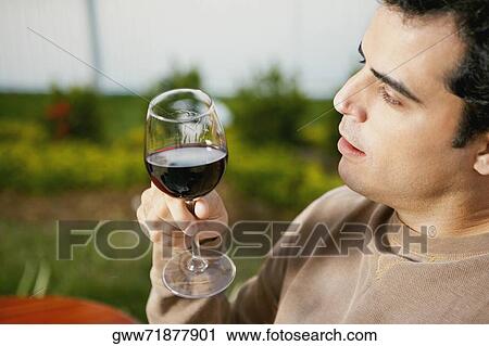 Stock Image - Side profile of a mid adult man holding a glass of red wine. Fotosearch