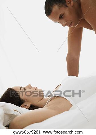 Stock Image - Side profile of a mid adult man looking at a young woman lying on the bed. Fotosearch