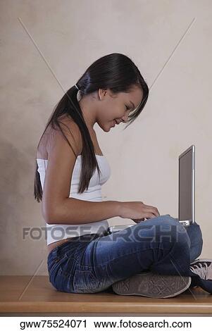 Stock Image - Side profile of a teenage girl sitting on the floor and using a laptop. Fotosearch