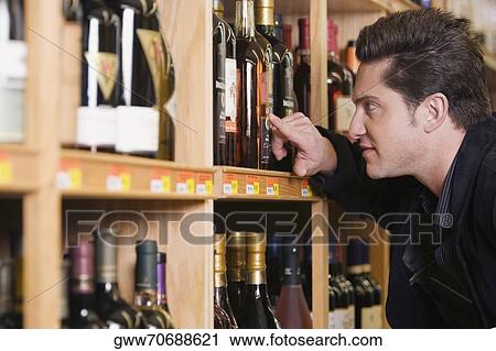 Side profile of a young man looking at a wine bottle in a liquor store View Large Photo Image Stock Image - Side profile of a young man looking at a wine bottle in a liquor store. Fotosearch