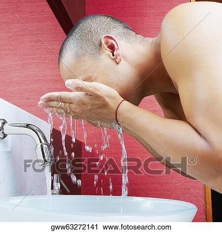 Stock Image - Side profile of a young man washing his face in the bathroom sink. Fotosearch