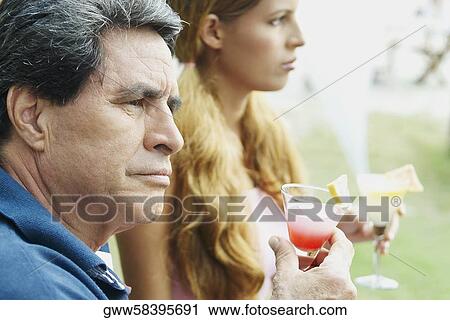 Stock Image - Side profile of a young woman and a mature man holding glasses. Fotosearch