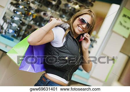 Side profile of a young woman carrying shopping bags and using a mobile phone View Large Photo Image Stock Image - Side profile of a young woman carrying shopping bags and using a mobile phone. Fotosearch
