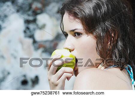 Stock Image - Side profile of a young woman eating a green apple. Fotosearch