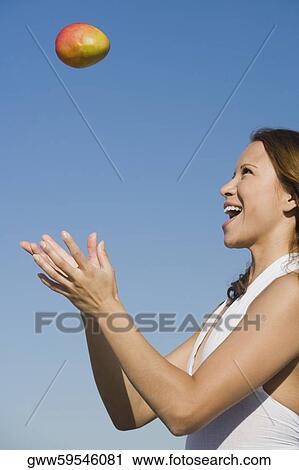 Side profile of a young woman tossing a mango View Large Photo Image Stock Image - Side profile of a young woman tossing a mango. Fotosearch