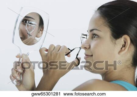 Stock Image - Side profile of a young woman using an eyelash curlers. Fotosearch