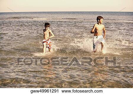 Teenage boy running in water with his brother View Large Photo Image Stock Image - Teenage boy running in water with his brother. Fotosearch