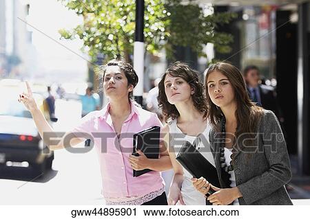 Three businesswomen hailing a taxi at the roadside View Large Photo Image Stock Image - Three businesswomen hailing a taxi at the roadside. Fotosearch