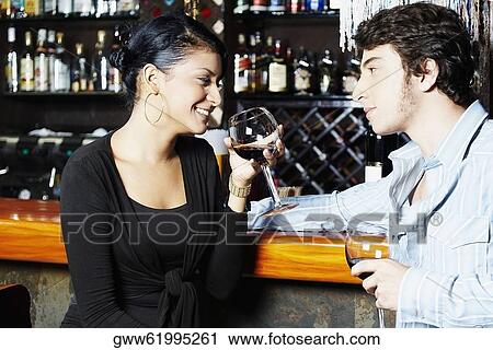 Stock Image - Young couple holding glasses of wine and looking at each other. Fotosearch