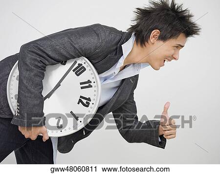 Young man holding a clock and making a thumbs up sign View Large Photo Image Stock Image - Young man holding a clock and making a thumbs up sign. Fotosearch