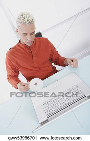 Young man sitting in front of a laptop and holding a CD View Large Photo Image Stock Image - Young man sitting in front of a laptop and holding a CD. Fotosearch