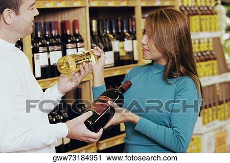 Young woman and a mid adult man looking at each other and holding wine bottles View Large Photo Image Stock Image - Young woman and a mid adult man looking at each other and holding wine bottles. Fotosearch