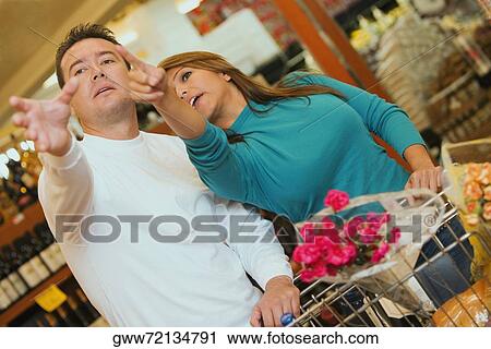 Young woman and a mid adult man standing in a supermarket and pointing forwards View Large Photo Image Stock Image - Young woman and a mid adult man standing in a supermarket and pointing forwards. Fotosearch