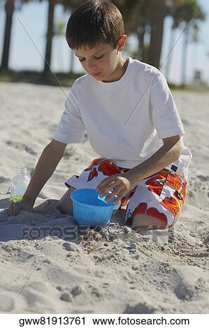 Boy crouching and playing with sand on the beach View Large Photo Image Stock Image - Boy crouching and playing with sand on the beach. Fotosearch