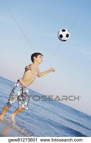 Stock Image - Boy playing soccer on the beach. Fotosearch