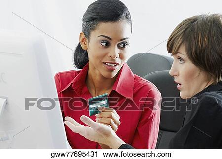 Businesswoman holding a credit card with another sitting beside her in front of a computer View Large Photo Image Stock Image - Businesswoman holding a credit card with another sitting beside her in front of a computer. Fotosearch