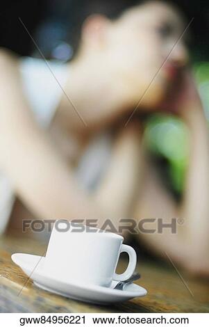 Stock Image - Close-up of a cup and a saucer with a woman in the background. Fotosearch