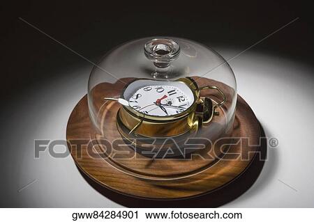 Stock Image - Close-up of a glass container covering an alarm clock on a dish. Fotosearch