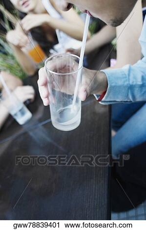 Stock Image - Close-up of a man drinking a glass of soda with a drinking straw. Fotosearch