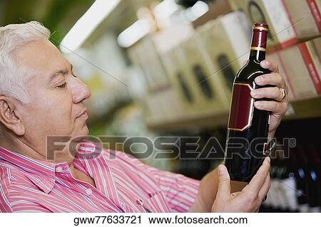 Close-up of a mature man holding a bottle of wine in a supermarket View Large Photo Image Stock Image - Close-up of a mature man holding a bottle of wine in a supermarket. Fotosearch