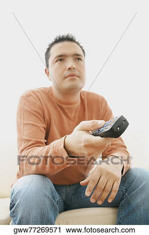 Stock Image - Close-up of a mid adult man sitting on couch and operating a remote control. Fotosearch